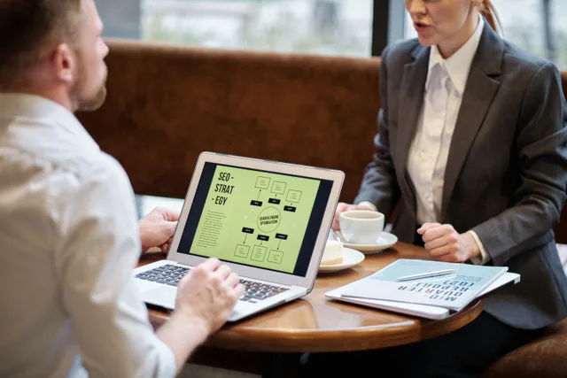 A man and woman engaged in a business meeting discussing SEO strategy in a cozy cafe setting. Should you hire a keyword research agency without a controlled pilot first?
