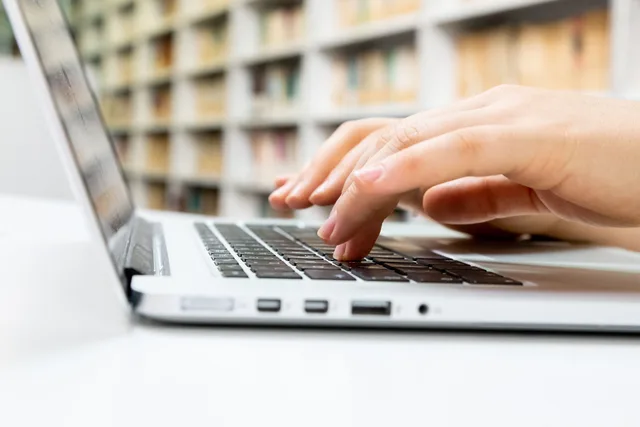Close-up of hands typing on a laptop keyboard in a library setting. Common keyword research questions: working answers and a decision record