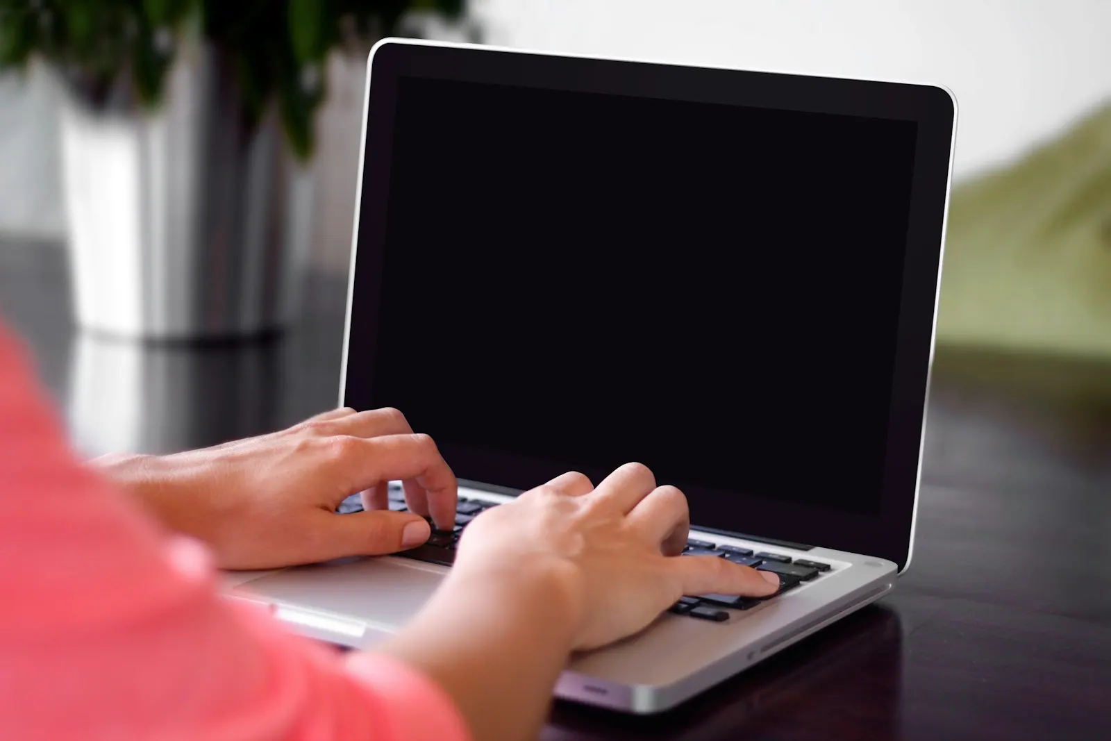 person wearing pink shirt typing on gray laptop computer on desk Typing on a laptop. When cutting old pages improves rankings: a content pruning SEO strategy