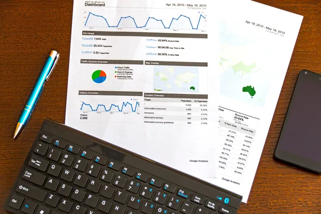 Flatlay of a business analytics report, keyboard, pen, and smartphone on a wooden desk. Technical SEO benchmarks compared on inventory, rendering, and recovery