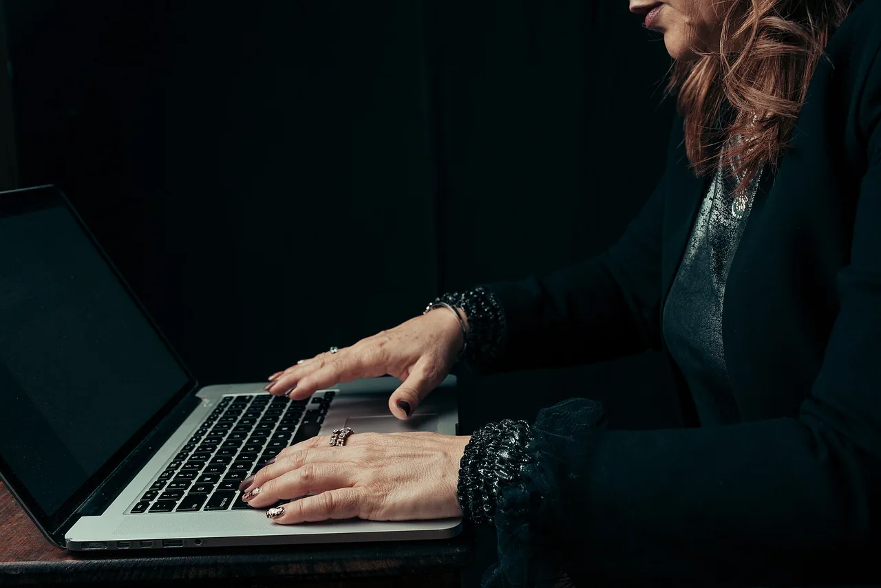 A woman concentrating as she types on a laptop in a dim workspace.